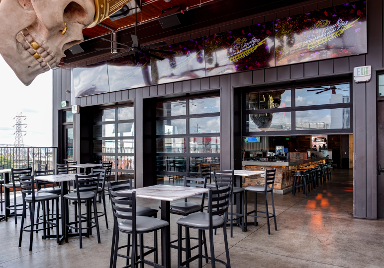 rooftop-bar-with-clopay-glass-garage-doors-Nashville A rooftop bar patio with black high-top tables and a giant decorative skull, featuring black-framed Clopay full-view glass garage doors that open to the interior bar.